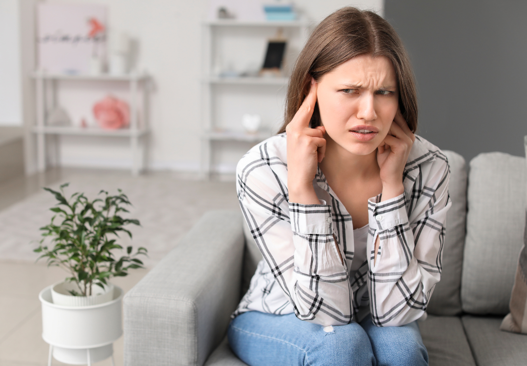 woman sitting on a couch plugging her ears